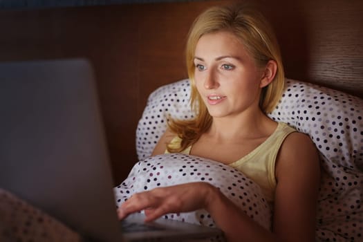 A young woman working on her laptop while lying in bed