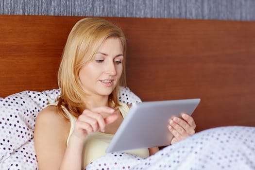 A young woman working on her tablet while lying in bed