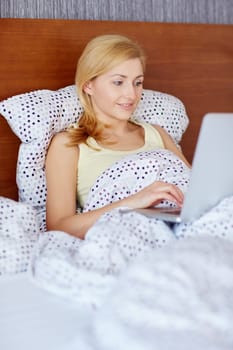A young woman working on her laptop while lying in bed