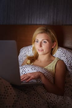 A young woman working on her laptop while lying in bed