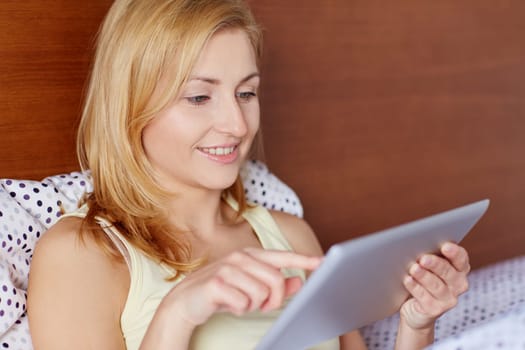 A young woman working on her tablet while lying in bed