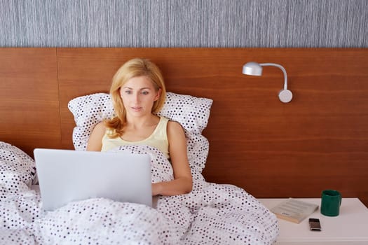 A young woman working on her laptop while lying in bed