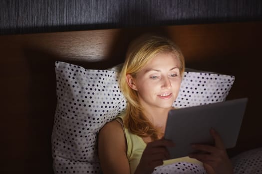 A young woman working on her tablet while lying in bed