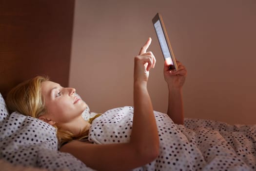 A young woman working on her tablet while lying in bed