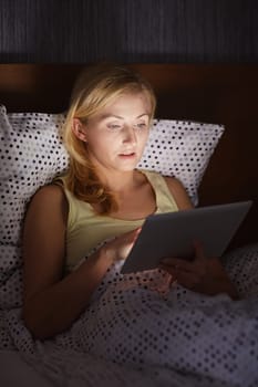 A young woman working on her tablet while lying in bed