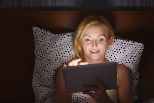 A young woman working on her tablet while lying in bed