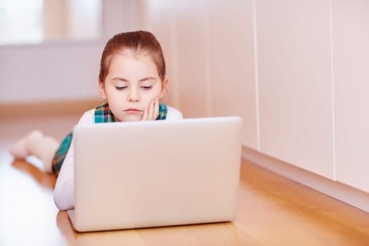 A cute little girl looking bored while playing on a laptop