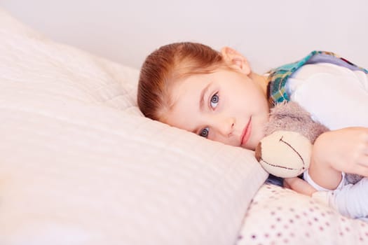 A cute little girl lying on her bed with her teddy