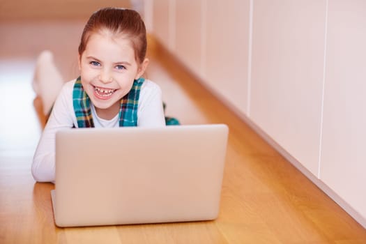 A cute little girl smiling at the camera while playing on a laptop