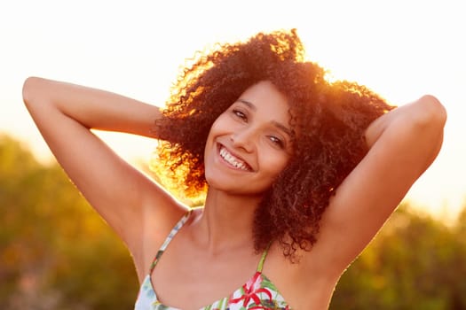 Beautiful mixed race woman happily smiling in a park on a summer evening with golden sun light