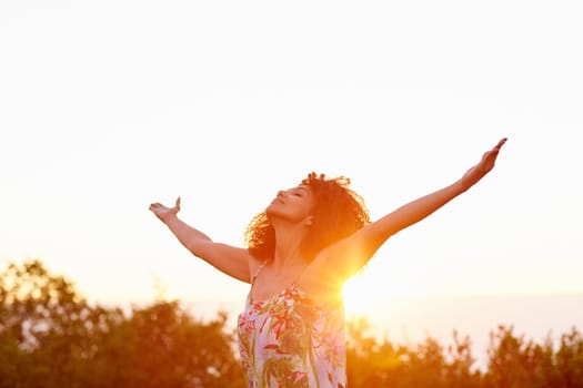 A beautiful young woman with arms outstretched at sunset