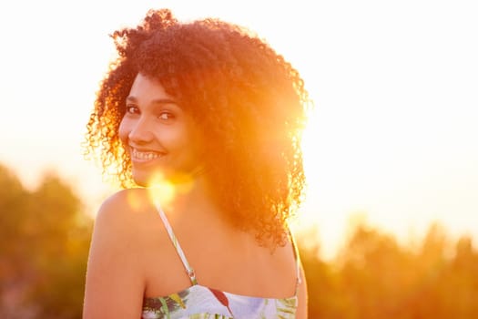 Beautiful mixed race woman looking back over her shoulder happily smiling at the camera with goldern sun flare