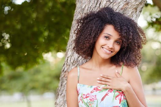 Beautiful young mixed race woman giving a shy smile in a green park outdoors