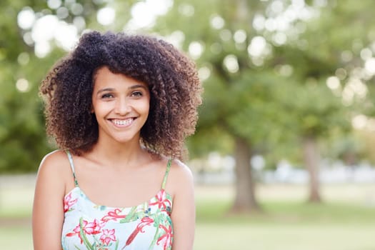 A young woman standing a park with trees behind her