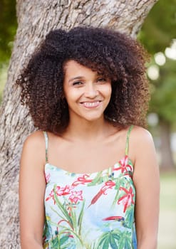 Beautiful mixed race woman happily smiling at the camera while leaning against a tree trunk in a park