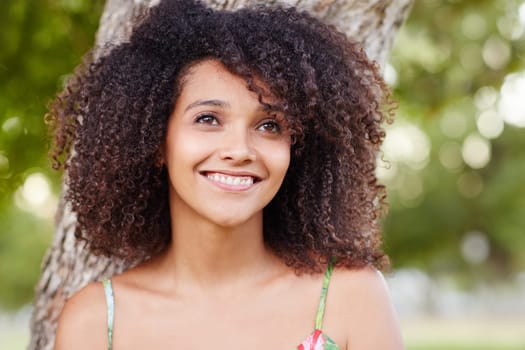 A young woman standing a park with trees behind her