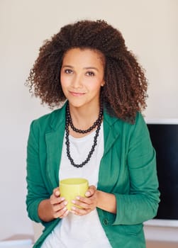 A young businesswoman holding a coffee cup while leaning against her desk