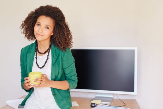 A young businesswoman holding a coffee cup while leaning against her desk