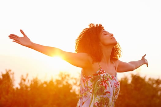 Beautiful mixed race woman expressing freedom on a summer evening outdoors with her arms outstretched