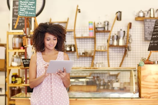 Beautiful cafe owner running her small business with the help of a digital tablet while standing near the counter of her coffee shop