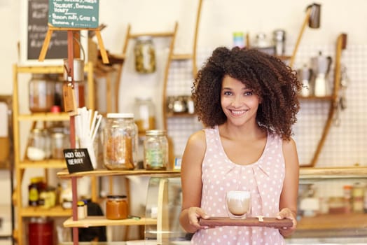 Beautiful young mixed race waitress carrying a latte in a modern glass mug on a wooden tray