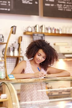 Beautiful young woman with an afro hairstyle writing down and order at the counter of a coffee shop