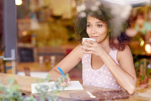 Beautiful mixed race woman sitting in a coffee shop sipping her latte and daydreaming while gazing out of the window