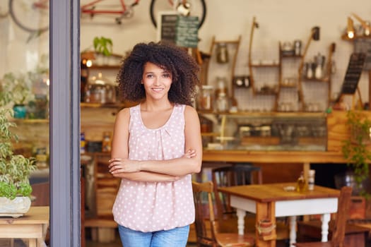 Beautiful young cafe owner proud of her small business standing smiling in the doorway of her coffee shop