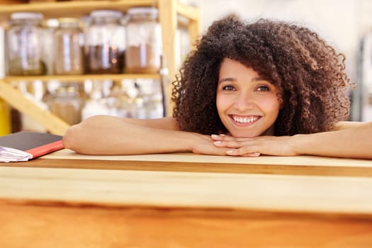 Pretty mixed race waitress in a coffee shop, leaning on a wooden counter