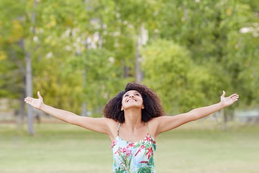 Beautiful young woman standing in a park celebrating her freedom by stretching her arms out in a natural setting