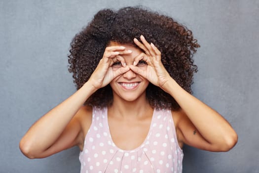 A young woman looking at you through her fingers against a gray background