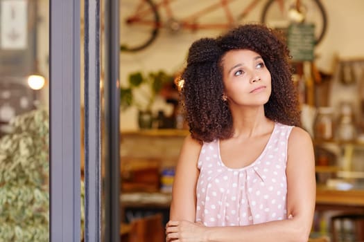 Beautiful young woman standing in the doorway of her coffee shop thinking about the future of her small business