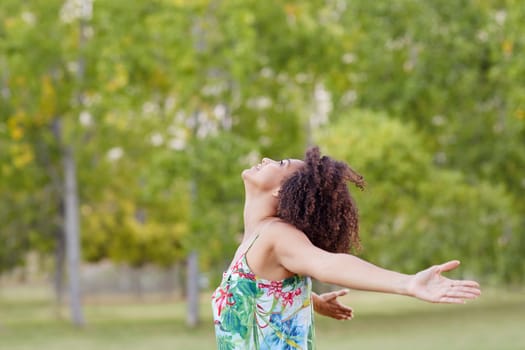 Mixed race woman stretching her arms out in a pose of freedom in a green park setting