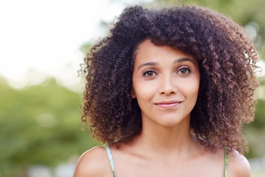 Closeup of a young woman standing a park with trees behind her