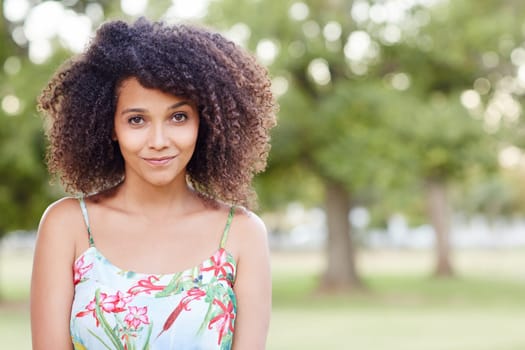 Pretty young mixed race woman smiling sweetly at the camera in a green park
