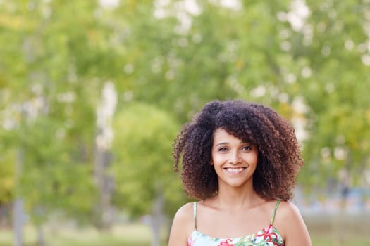 A young woman standing a park with trees behind her