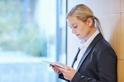 A young businesswoman reading her tablet while leaning against a wall