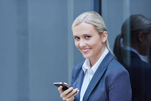 A young businesswoman typing an sms on phone with glass behind her