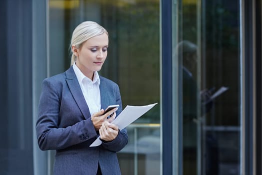 A young businesswoman texting someone outside a building