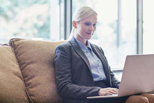 A young businesswoman working on her laptop while sitting on a sofa