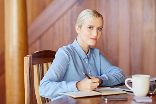 A young businesswoman taking notes in wooden office, looking in to the camera