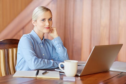 A young businesswoman at her desk, looking in to the camera inside wooden office