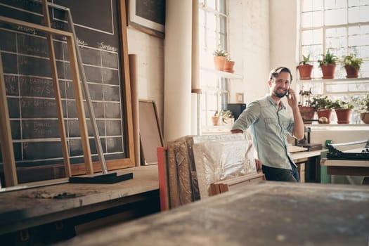 Small business owner talking on his phone while smiling and standing casually in his studio workshop