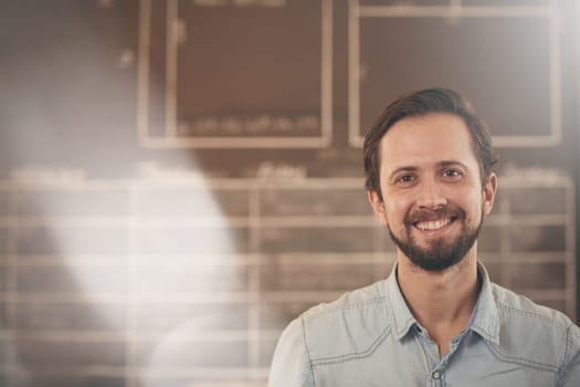 Head and shoulders portrait of a handsome craftsman and designer in his studio smiling at the camera