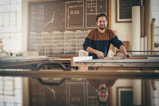 Skilled craftsman looking up from his work and smiling while standing in his studio busy with a woodwork project