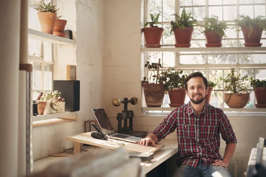 Young male designer sitting comfortably in his office space in his studio which has beautiful natural light and many plants
