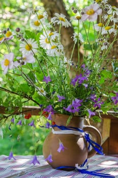 Jug with a bouquet of summer flowers on a table in the garden, close up