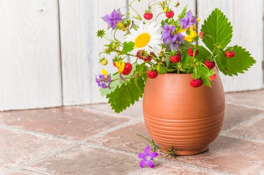 Ripe strawberries and a bouquet of forest flowers in a clay mug