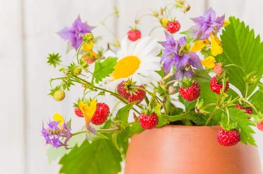 Ripe strawberries and a bouquet of forest flowers in a clay mug