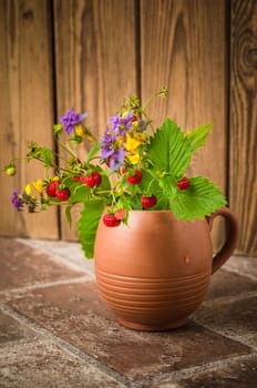 Ripe strawberries and a bouquet of forest flowers in a clay mug
